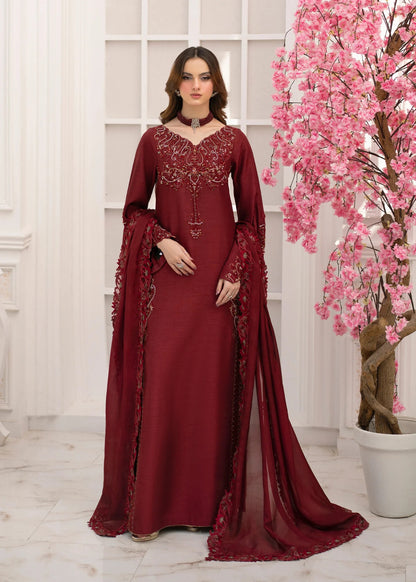 Woman in a burgundy embroidered dress standing next to a pink flowering tree indoors.