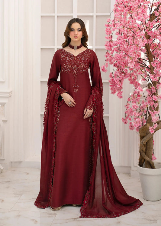Woman in a burgundy embroidered dress standing next to a pink flowering tree indoors.