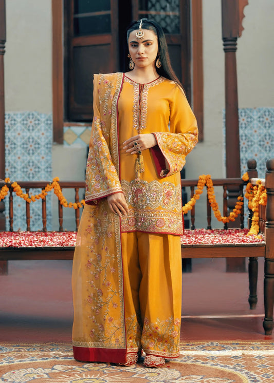 Woman in traditional yellow and red embroidered outfit standing in a decorated room.
