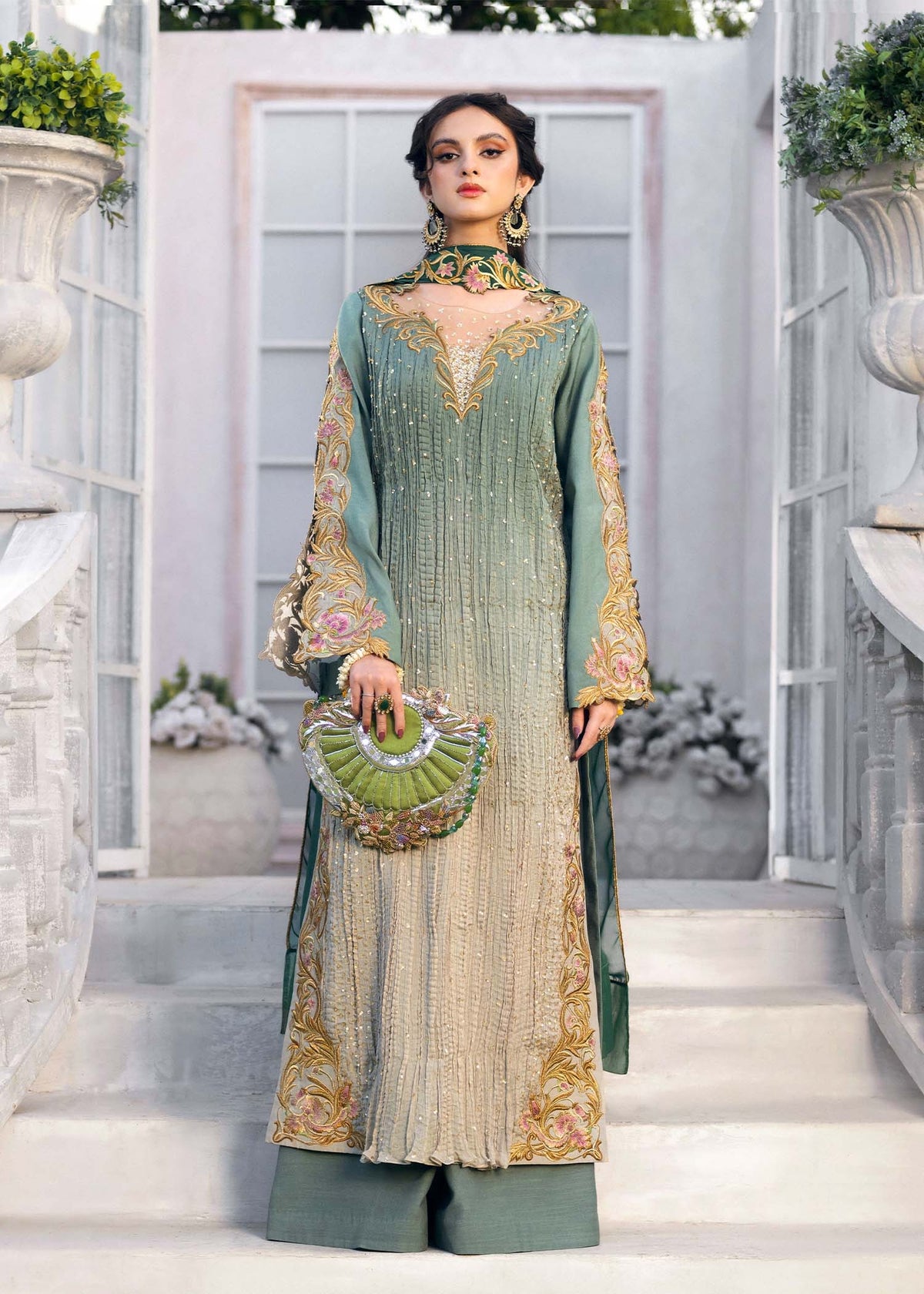 Woman in a green and beige embroidered outfit standing in an elegant outdoor setting.