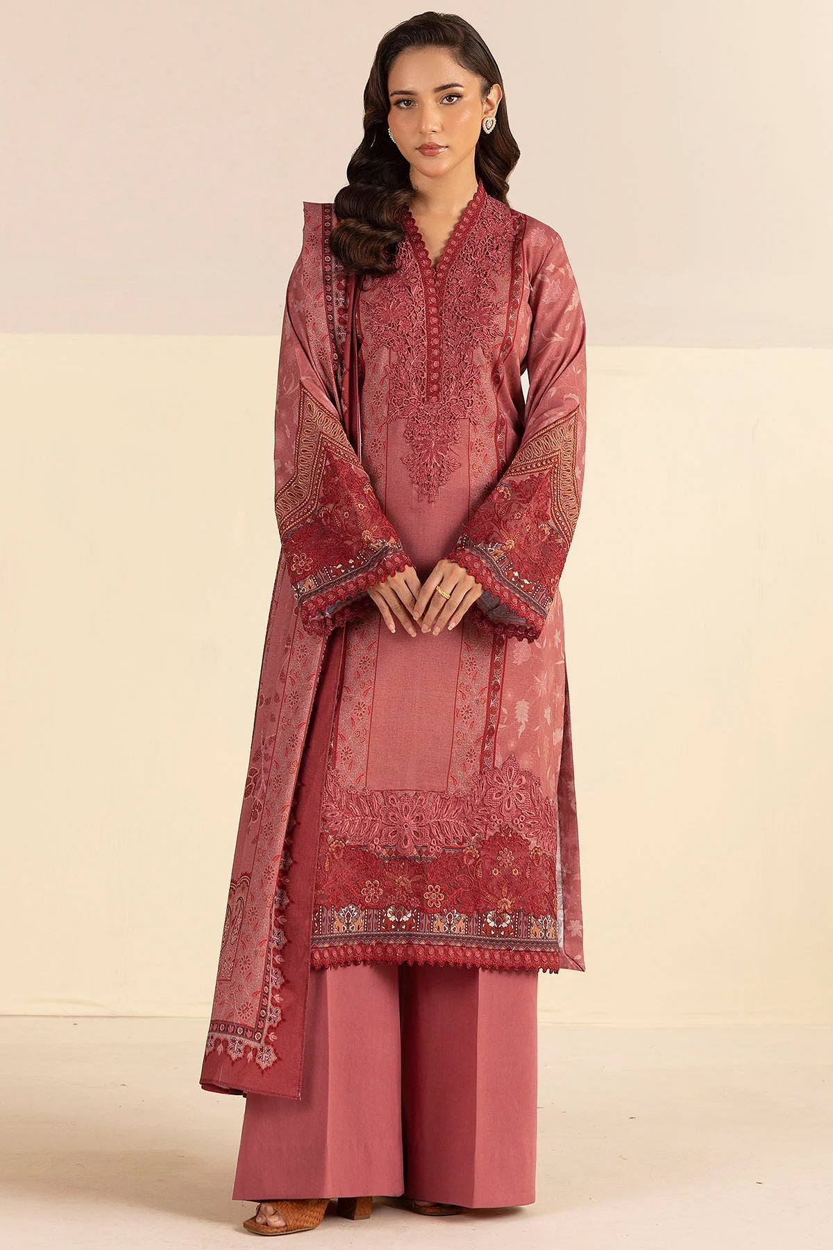 Woman wearing a traditional pink embroidered outfit on a beige background