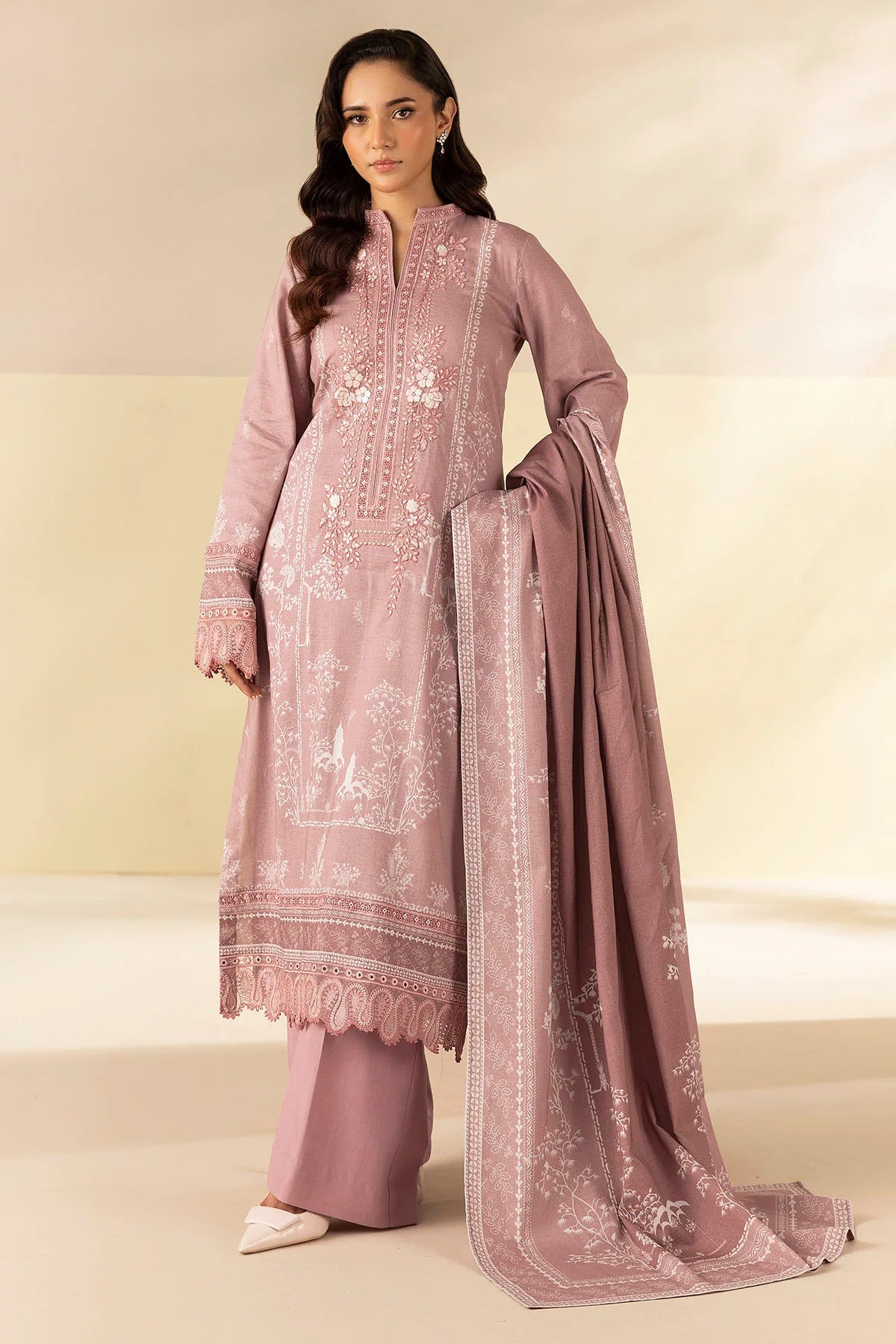 Woman wearing a pink embroidered traditional outfit with a matching dupatta on a beige background