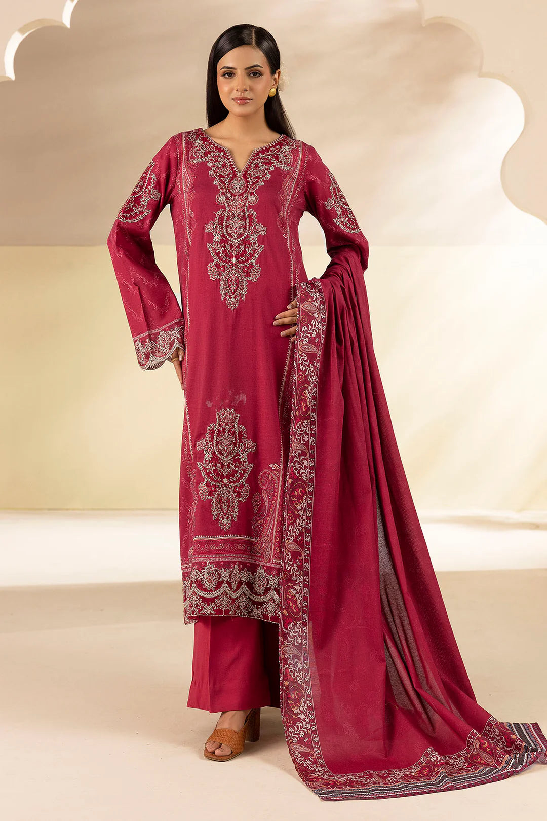 Woman wearing a maroon embroidered traditional outfit with a matching dupatta on a beige background