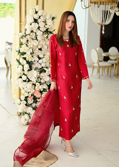 Woman in a deep red silk dress by allure standing in a decorated room with flowers and furniture.
