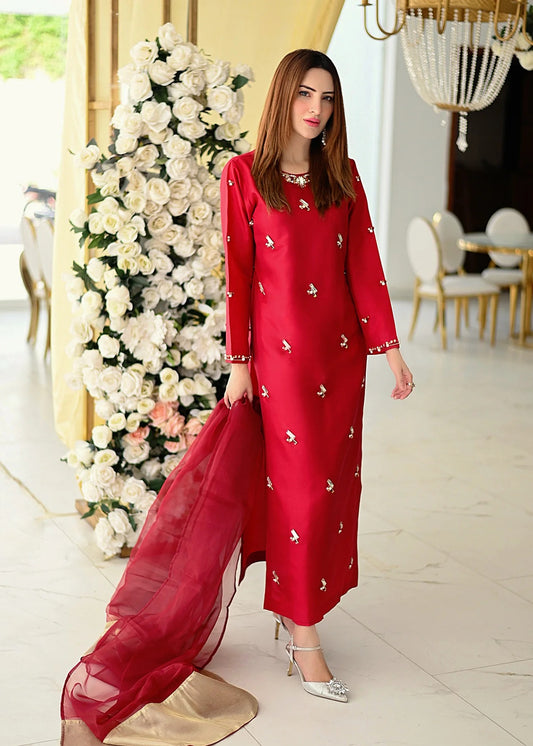 Woman in a deep red silk dress by allure standing in a decorated room with flowers and furniture.